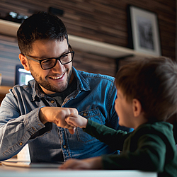 Vater und Sohn geben sich die Faust und lachen sich dabei an.