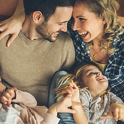 Eltern toben mit ihren beiden Kindern auf einem Sofa.