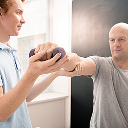 Ein junger Physiotherapeut hilft einem Patienten beim Heben und Dehnen des Arms mit Hantel.