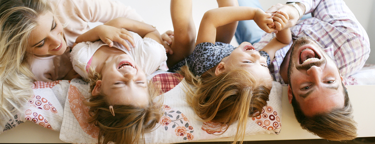 Mutter, Vater und beide Töchter liegen glücklich, kopfüber im Bett