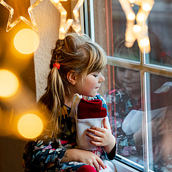 Ein kleine Mädchen schaut aus einem Fenster und hat einen Nikolausstiefel auf dem Schoß.