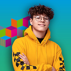 Ein junger Mann mit braunen lockigen Haaren und Brille lacht in die Kamera. Er trägt einen gelben Pullover. 