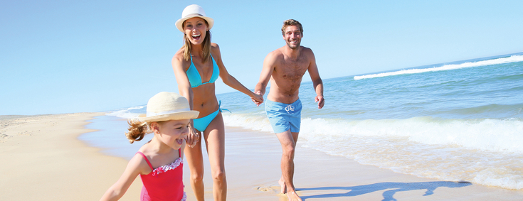 Auslands-Krankenversicherung Mutter. Vater. Tochter laufen Hand in Hand glücklich am Strand