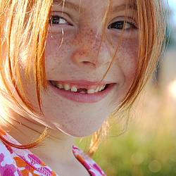 Ein junges Mädchen mit langen roten Haaren und Sommersprossen lacht fröhlich.