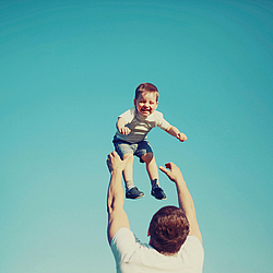 Ein Mann wirft einen kleinen Jungen in die Luft. Der Junge lacht dabei vor Freude.