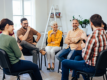 Mehrere Personen sitzen in einem Kreis auf Stühlen und unterhalten sich.