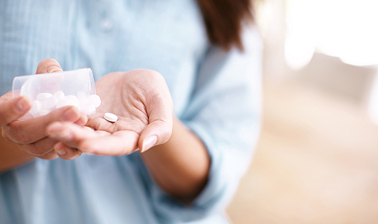 Eine Frau hält eine kleine Dosen mit Tabletten in der Hand und schüttet sich eine Pille in die offene Handfläche.