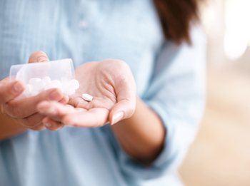 Eine Frau hält eine kleine Dosen mit Tabletten in der Hand und schüttet sich eine Pille in die offene Handfläche.