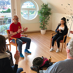 Mehrere Personen sitzen in einem Stuhlkreis. Sie führen eine Entspannungsübung durch.