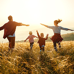 Familie läuft über ein Feld bei Sonnenuntergang.