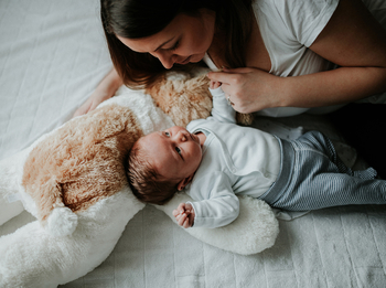 Mutter mit Baby auf dem Bett und Kuscheltier