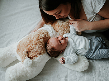 Eine junge Mutter liegt mit ihrem Säugling auf dem Bett. Die beiden schauen sich liebevoll an. 