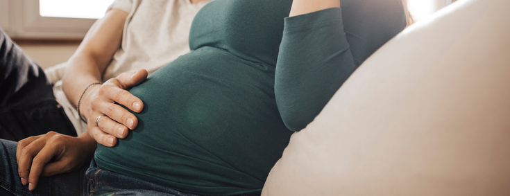 Schwangerschaftsvorsorge Paar glücklich Mann legt Hand auf schwangeren Bauch von Frau