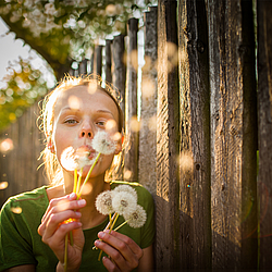 Eine blonde Frau hält Pusteblumen in ihren Händen und pustet die Samen in die Luft.