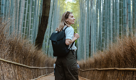 Eine Frau mit Rucksack geht einen Bambuswaldpfad entlang.