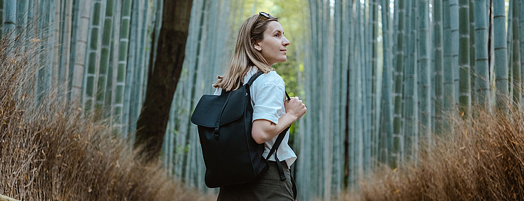 Eine Frau mit Rucksack geht einen Bambuswaldpfad entlang.