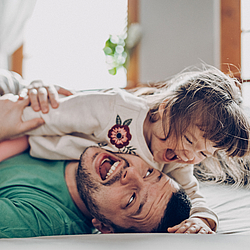 Vater und seine kleine Tochter toben auf dem Boden. Beiden lachen.