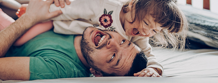 Vater und seine kleine Tochter toben auf dem Boden. Beiden lachen.