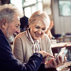 Eine ältere Frau und ein älterer Mann schauen gemeinsam auf ein Smartphone.