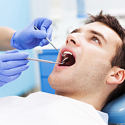 Ein Mann liegt auf einem Behandlungsstuhl bei einem Zahnarzt. Er hat den Mund weit geöffnet, während seine Zähne untersucht werden.