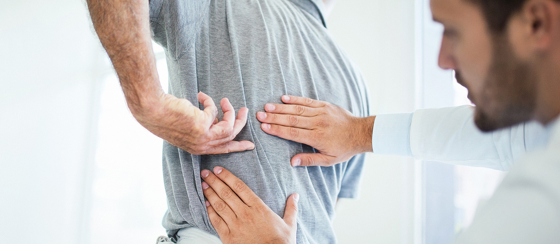 Ein Arzt untersucht mit seinen Händen den Rücken eines Mannes.