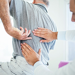 Ein Arzt untersucht mit seinen Händen den Rücken eines Mannes.