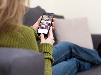 Eine Frau mit langen Haaren sitzt auf dem Sofa, man sieht über ihre Schulter auf ihr Handydisplay. Die Internetseite der BKK GS ist zu sehen.