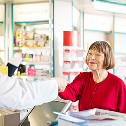 Eine ältere Frau bekommt in einer Apotheke etwas über den Tresen gereicht.