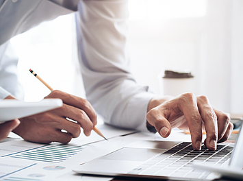 Auf Person steht an einem Schreibtisch. Sie macht Notizen und tippt etwas auf einem Lapotp.