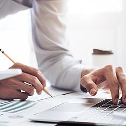 Auf Person steht an einem Schreibtisch. Sie macht Notizen und tippt etwas auf einem Lapotp.