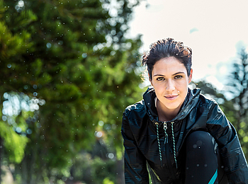 Eine dunkelhaarige Frau in Sportkleidung macht Dehnübungen im Park.