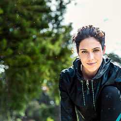 Eine dunkelhaarige Frau in Sportkleidung macht Dehnübungen im Park.