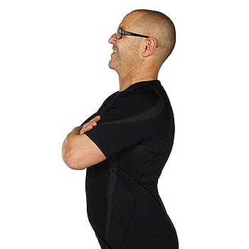 Ein Mann mit Brille trägt schwarze Kleidung. Er steht gerade und hat die Arme überkreuzt. Er zeigt die Übung Beckenwippe.