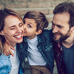 Mutter und Vater mit Kind. Das Kind gibt der Mutter ein Küsschen.