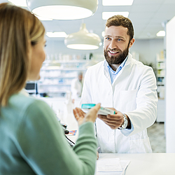 Ein Apotheker überreicht einer Kundin ein Medikament.