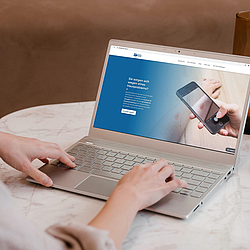 Eine Frau sitzt an einem Tisch, vor ihr steht ihr Laptop. Sie sucht nach Informationen auf der Internetseite von "Online Doctor".