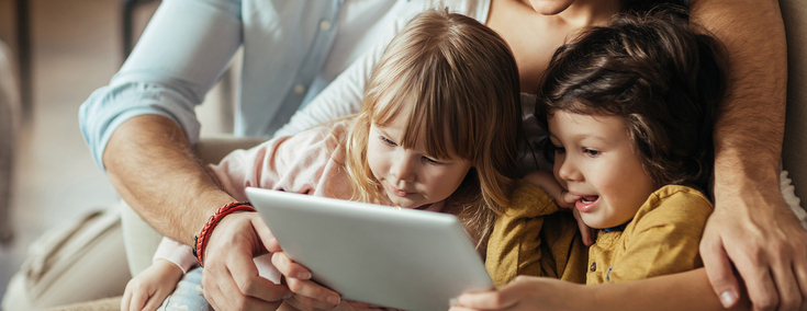 Mutter und Vater haben ihre beiden Kinder im Arm und schauen auf Tablet