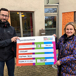 Eine Mitarbeiterin der BKK GILDEMEISTER SEIDENSTICKER und ein Mitarbeiter des Jugendhospiz in Bethel halten einen Spendenscheck.