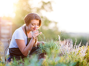 Frau im Garten riecht an Kräutern.