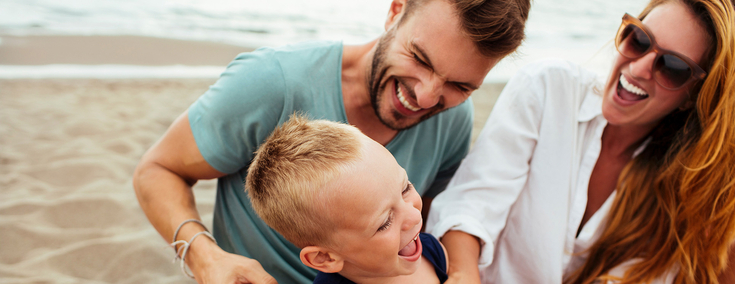 Mutter und Vater spielen glücklich mit Sohn am Strand