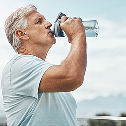 Ein Mann mit grauen Haaren trinkt aus einer Wasserflasche.