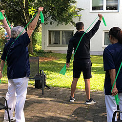 Zwei Personen bekommen Übungen mit einem Fitnessband vorgemacht und führen sie aus.