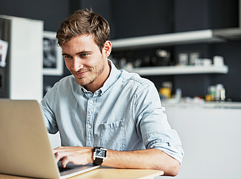 Ein Mann sitz in seiner Küche vor einem Laptop.