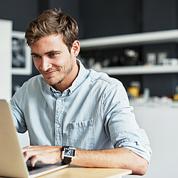 Ein Mann sitz in seiner Küche vor einem Laptop.