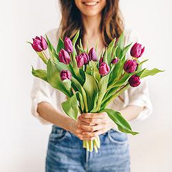 Eine Frau hält einen Strauß Tulpen. Sie lächelt dabei.
