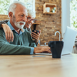 Ein älteres Paar sitzt gemeinsam an einem Tisch. Sie schauen auf einen Laptop.