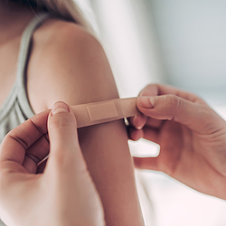 Ein junges Mädchen mit langen Haaren bekommt ein kleines Pflaster aus den Oberarm geklebt.