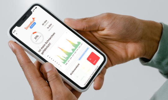 Ein Mann hält ein Smartphone. Auf dem Display sieht man die App von "Snorefox", diese zeigt die Ergebnisse eines Schlafapnoe-Tests.