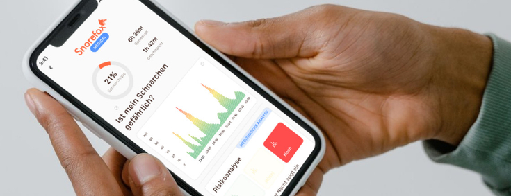 Ein Mann hält ein Smartphone. Auf dem Display sieht man die App von "Snorefox", diese zeigt die Ergebnisse eines Schlafapnoe-Tests.