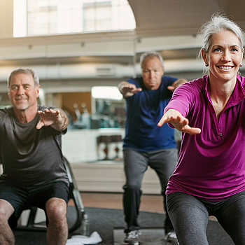 Eine Frau und zwei Männer machen gemeinsam Sportübungen in einem Fitnessraum.